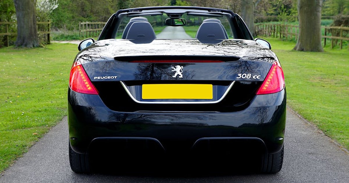 Rear view of a black Peugeot convertible on a countryside road in summer.