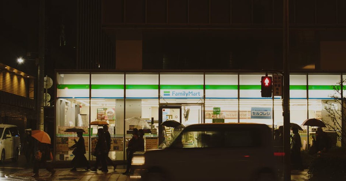 People crossing a street near a FamilyMart in Japan during a rainy night.