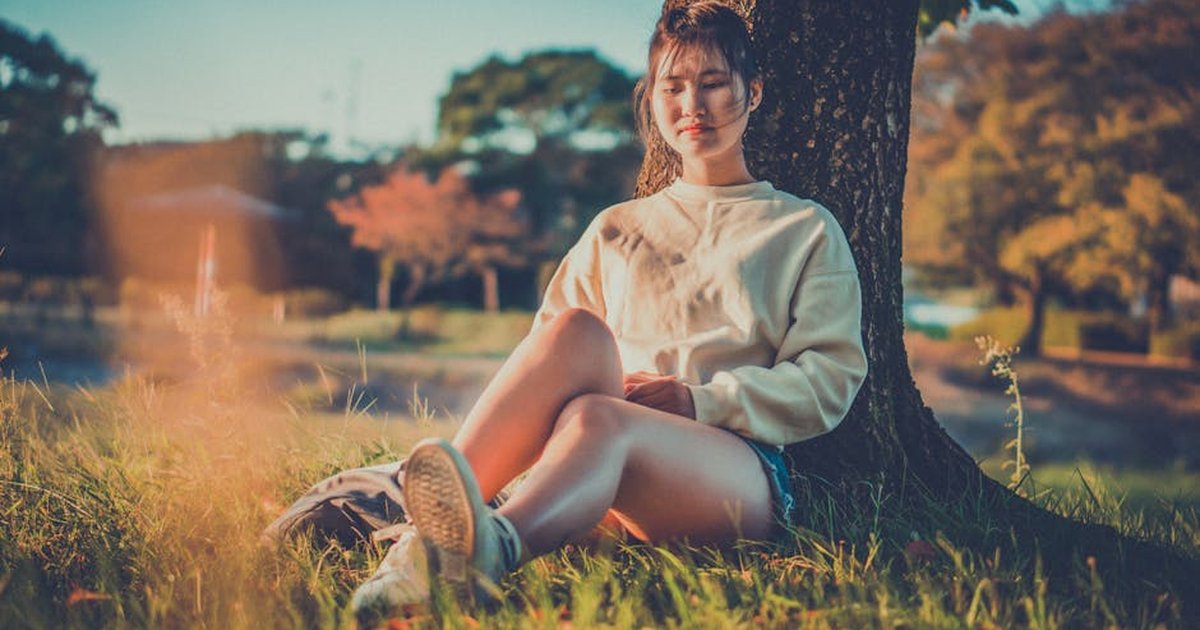 A serene moment captured as a young woman sits peacefully under a tree enjoying the outdoors.
