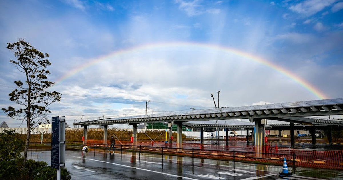 A vivid urban scene with a rainbow over a wet crosswalk under a blue sky.