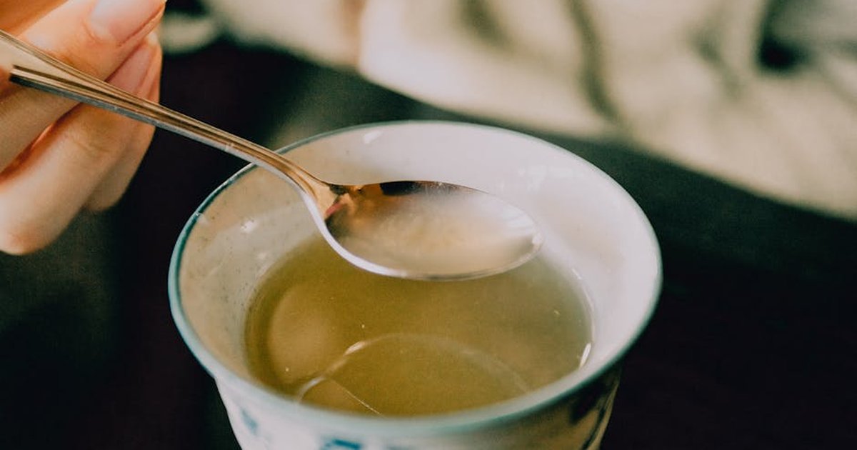 A hand holds a spoon over a cup of traditional Japanese green tea, offering a warm and soothing moment.