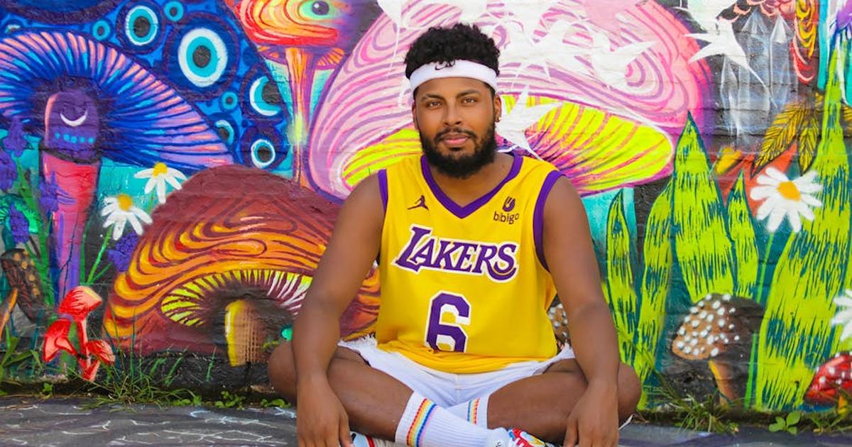 Man sitting against a vibrant mural wearing a Lakers jersey in São Paulo, Brazil.