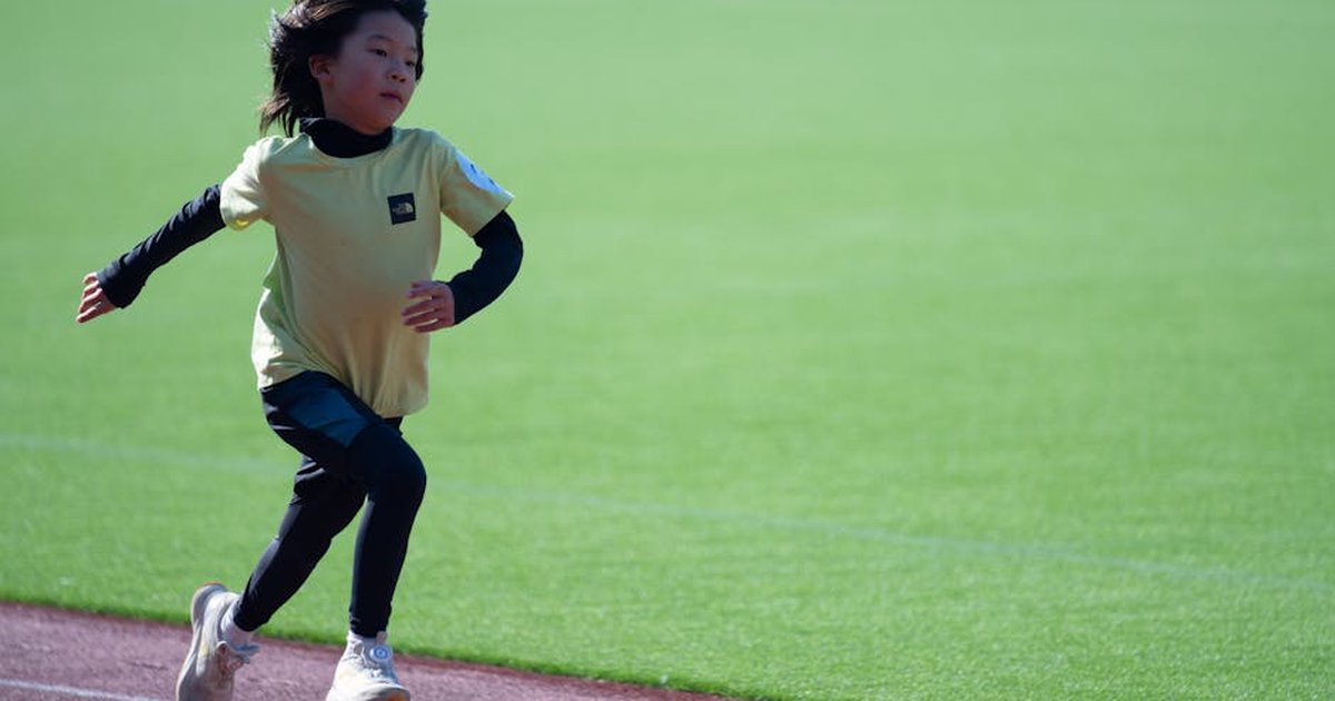 A young child running energetically on a track under sunny conditions.