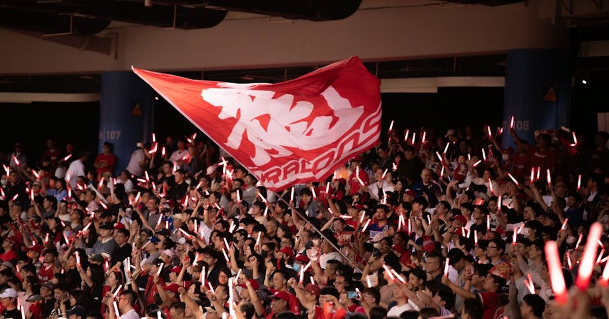 Vibrant crowd waving a flag with glowing sticks at a Taipei sports event, showcasing excitement and unity.