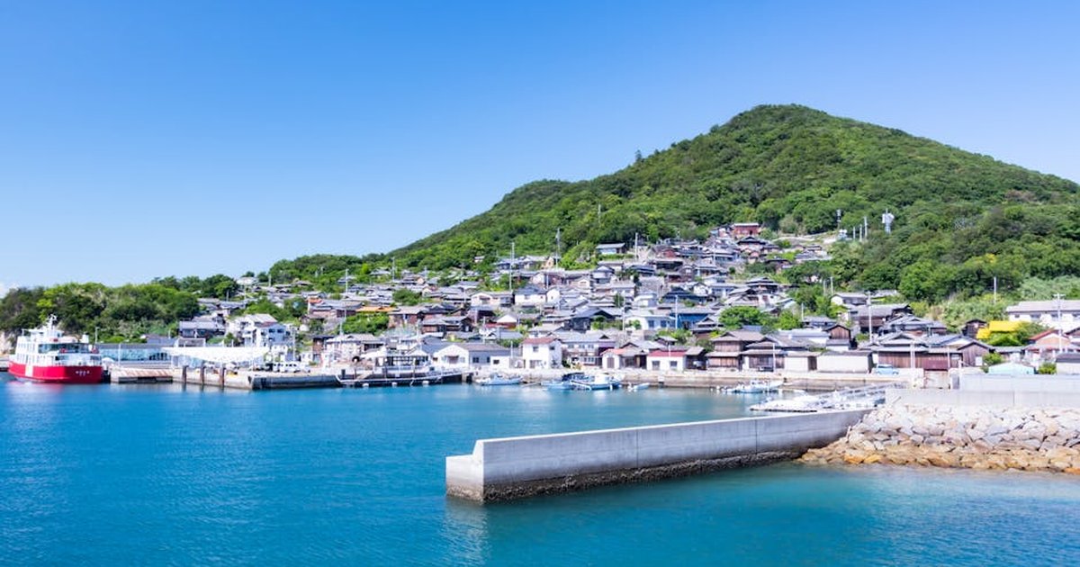 Idyllic Japanese village by the sea with boats, lush greenery, and clear skies.