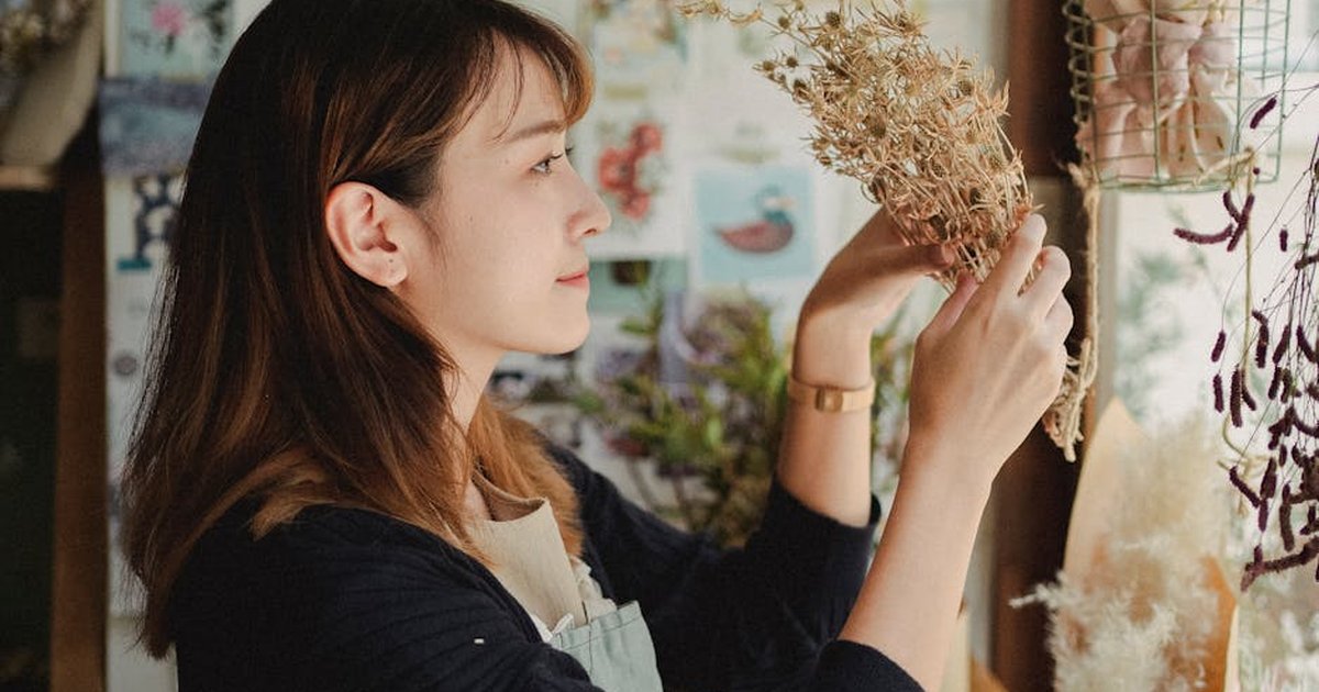 Side view of young woman in apron standing in floral shop and holding dry flowers