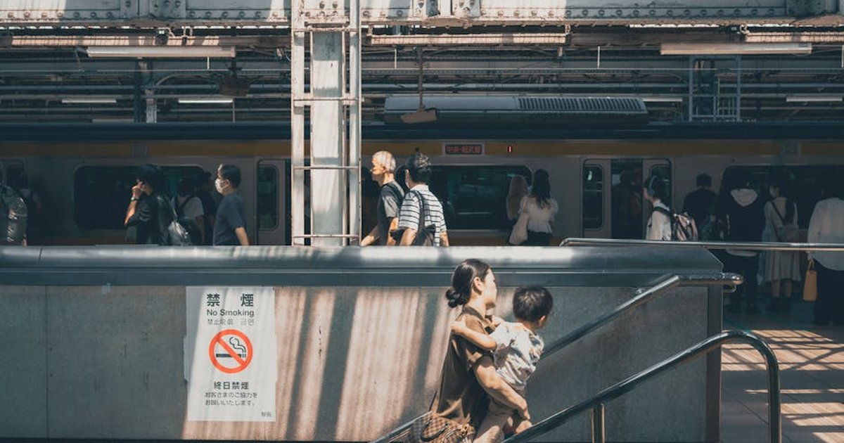 Commuters and a mother with child at a busy Tokyo train station, under sunlight.