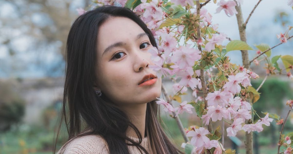 A serene portrait of a woman standing beside blossoming cherry trees in a springtime garden.