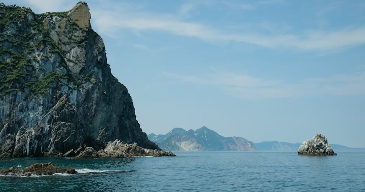 Tranquil ocean scene with towering rocky cliffs and clear blue sky.