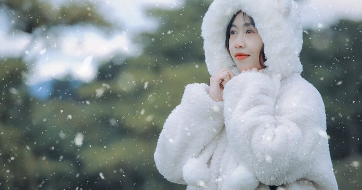 Woman enjoying a snowy day in a fluffy white fur coat outdoors in Vietnam.