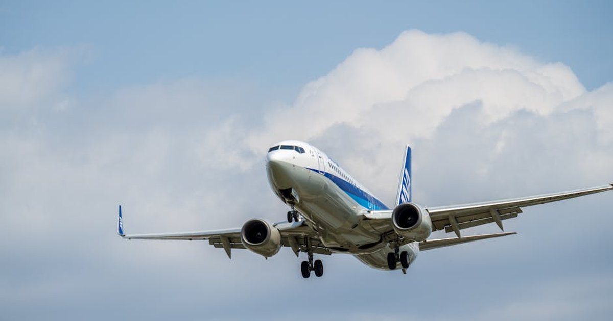 A commercial airplane ascending against a backdrop of blue sky and fluffy clouds, representing global travel.