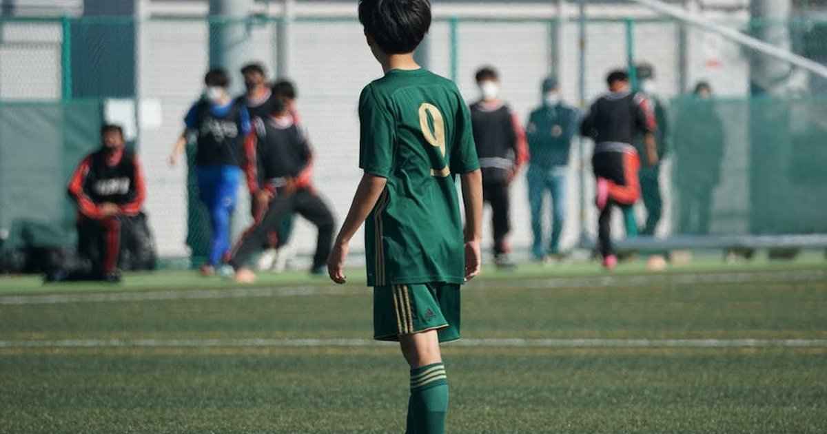 Youth soccer player in green jersey on football field during match.