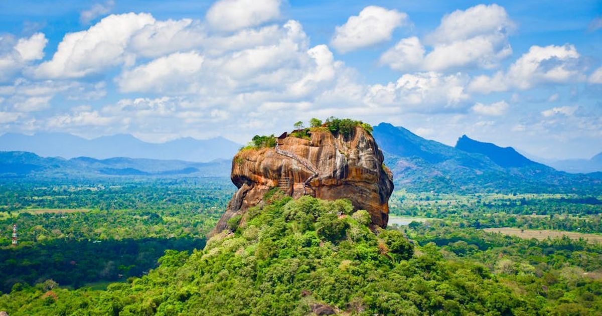 Explore the iconic Sigiriya Lion Rock surrounded by lush greenery and vibrant blue skies in Sri Lanka.