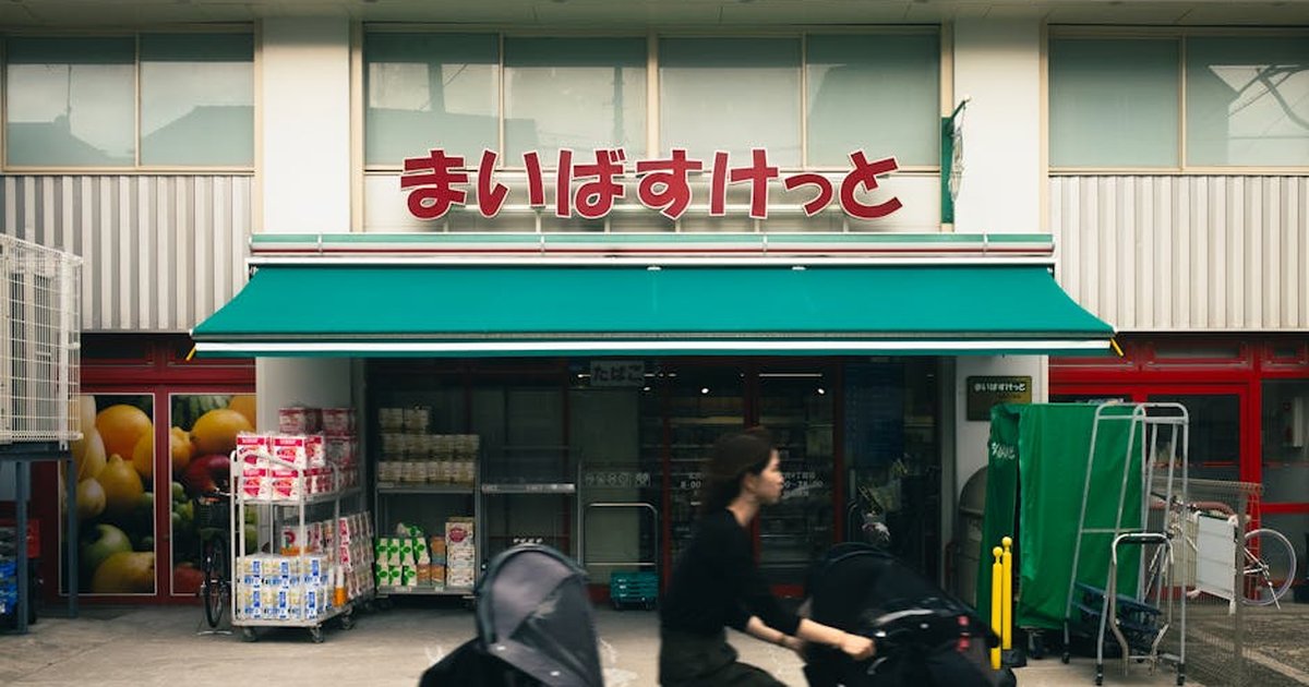 Woman rides bicycle past grocery store with Japanese signage in Tokyo.