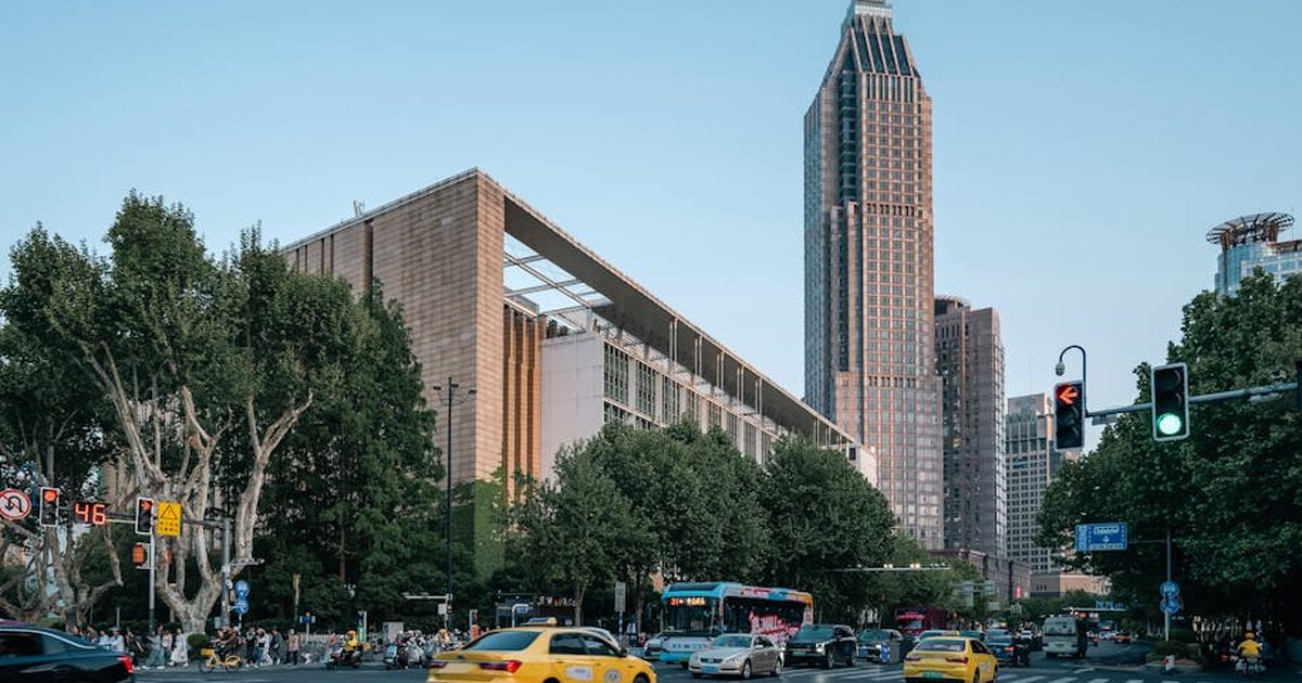 A bustling street scene near Nanjing Library with taxis and a towering skyscraper under a clear sky.
