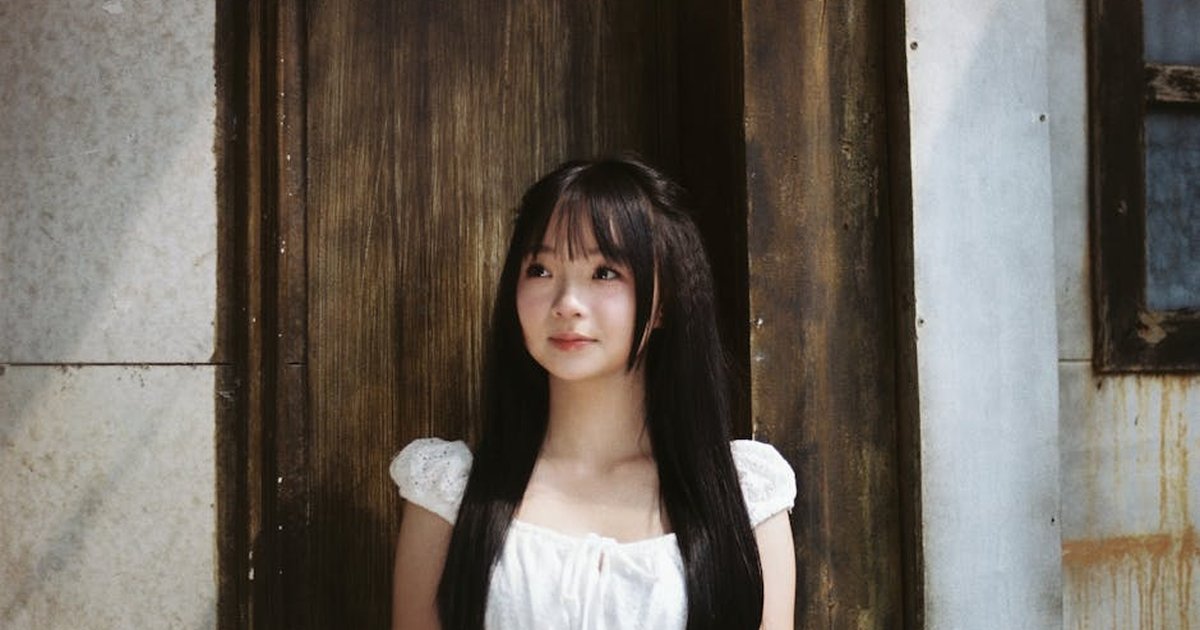 Young woman in a white dress stands by a rustic wooden door, creating a serene and classic portrait.