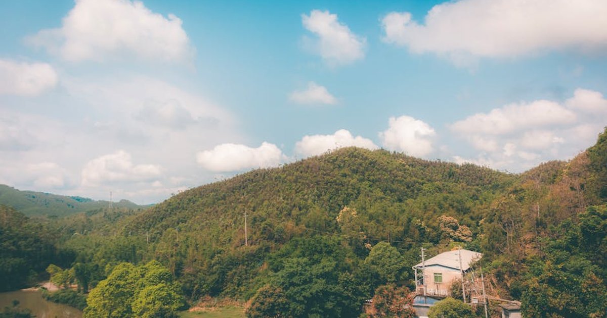 Scenic view of a rural Chinese landscape with a house, hills, and lush greenery under a bright blue sky.
