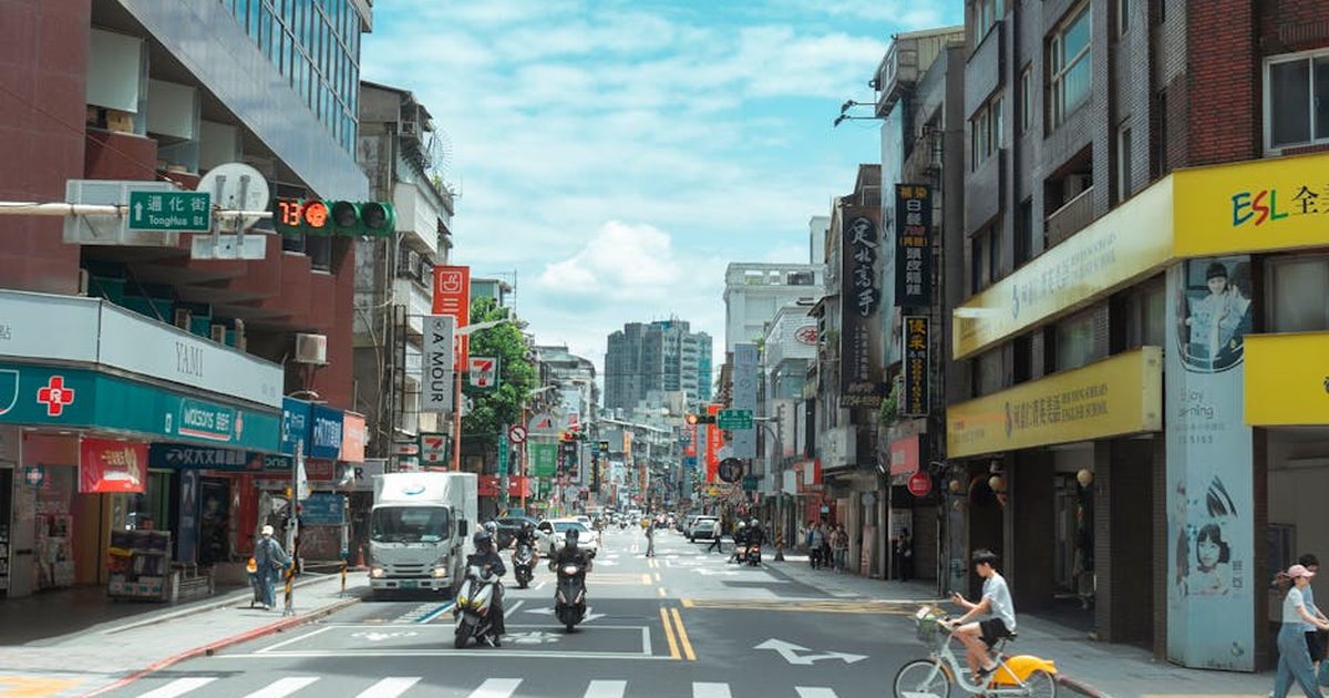 A bustling Taipei street with people, cars, and scooters under a bright sky in Taiwan.