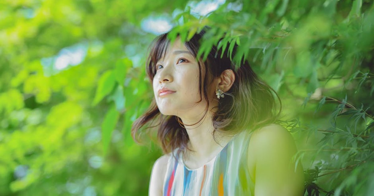 Smiling young woman with short brown hair in nature, surrounded by lush green leaves.