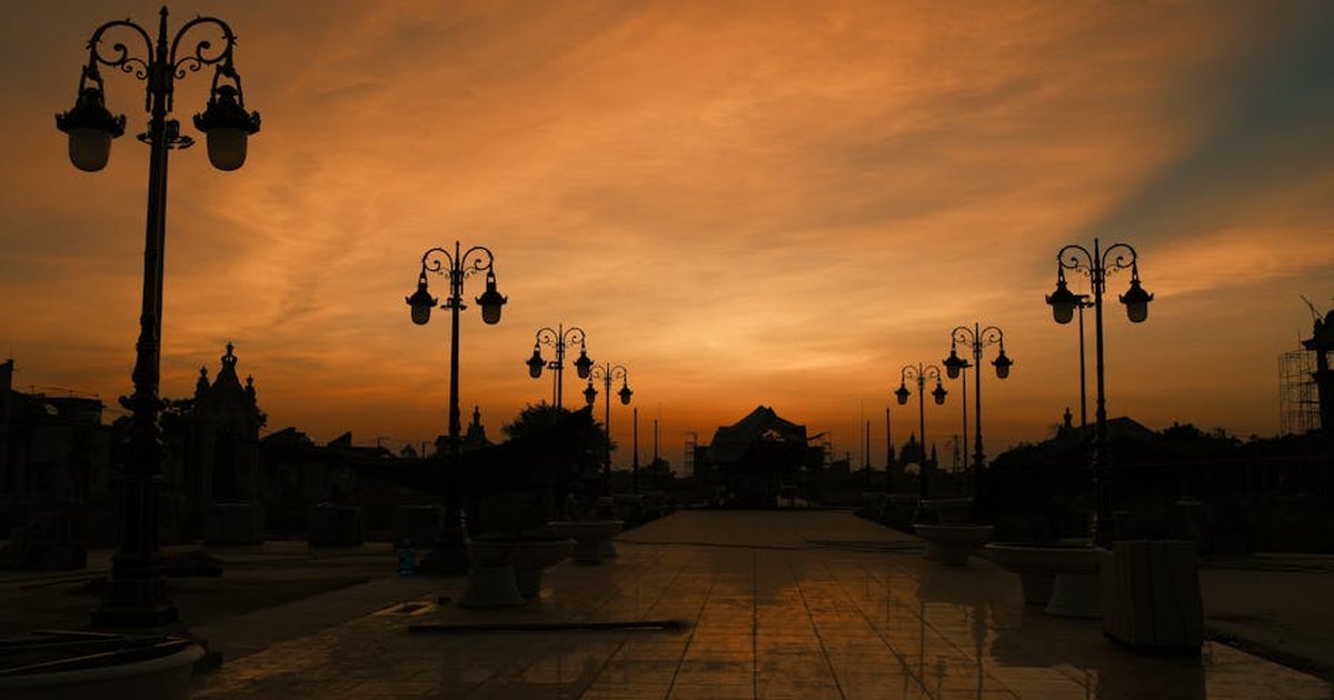Dramatic sunset sky with silhouette of vintage street lamps and architecture reflecting on tiles.