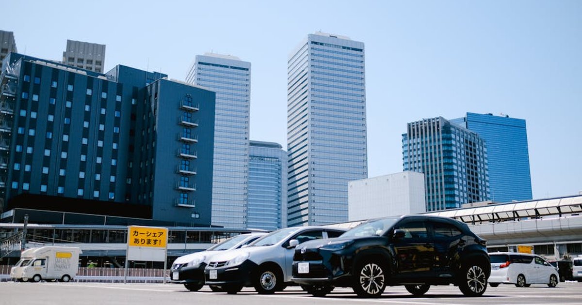 City parking lot with modern buildings and parked cars under a clear sky.