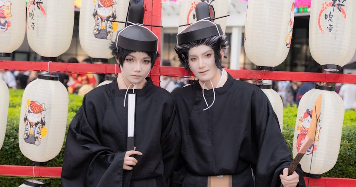 Two cosplayers in traditional attire during a vibrant Japanese festival with lanterns.