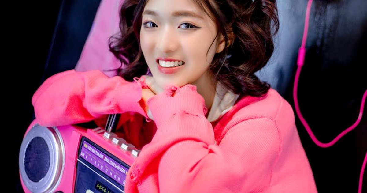 A young woman in bright pink fashion poses with a retro radio, smiling and vibrant.