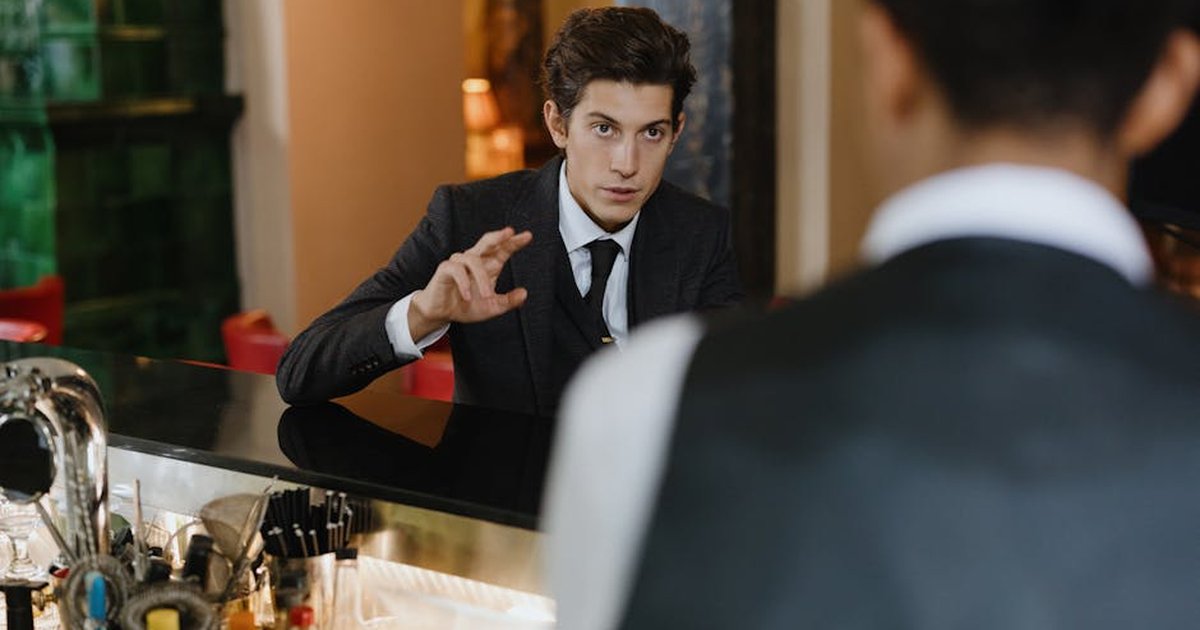 A classy interaction between a gentleman and a waiter at a stylish vintage bar setting.