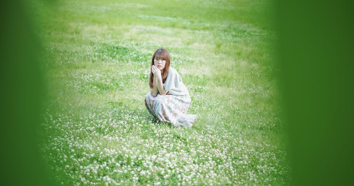 A serene outdoor scene with a woman sitting in a lush clover field, embracing natural beauty.