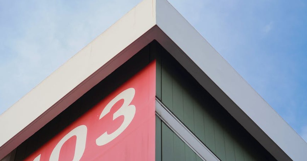 Close-up of a modern building corner with number 103 on a red panel against a blue sky.
