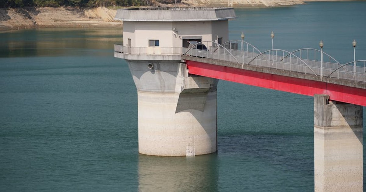 A concrete pier stands in a tranquil reservoir, showcasing industrial architecture against a summer backdrop.