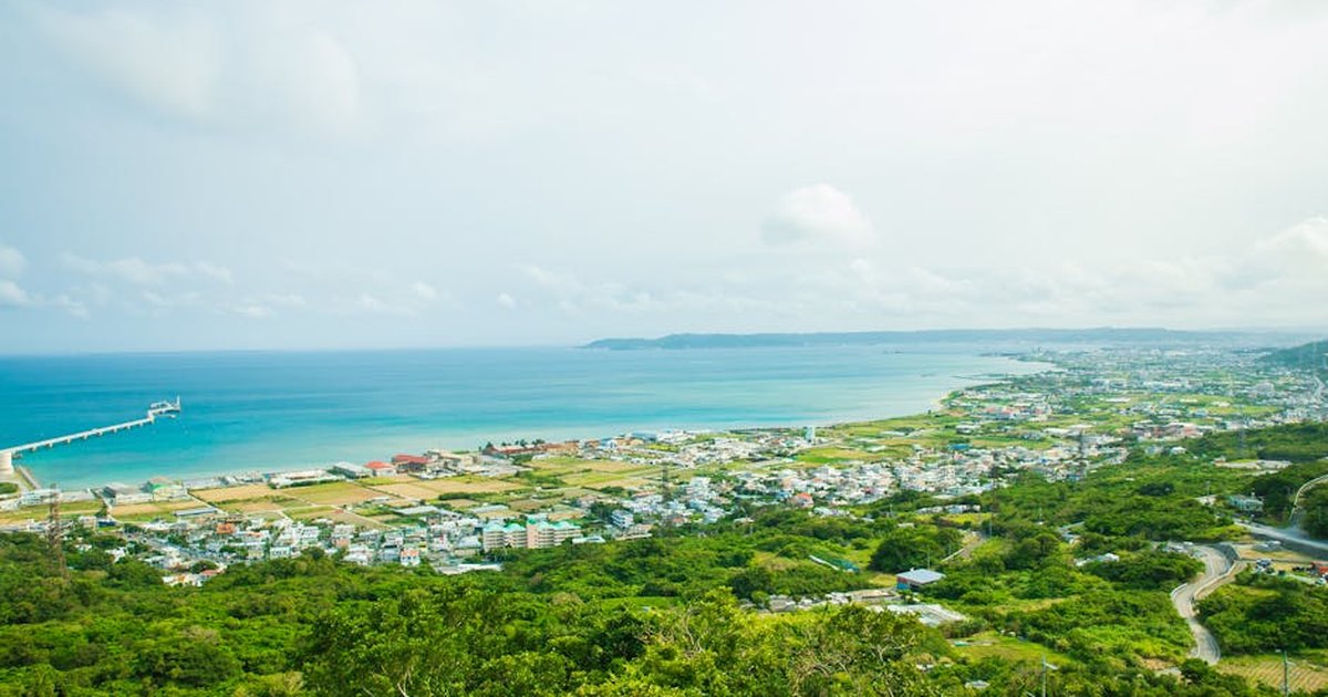 Calm turquoise water of ocean washing shore with small town and green tropical forest under cloudy sky