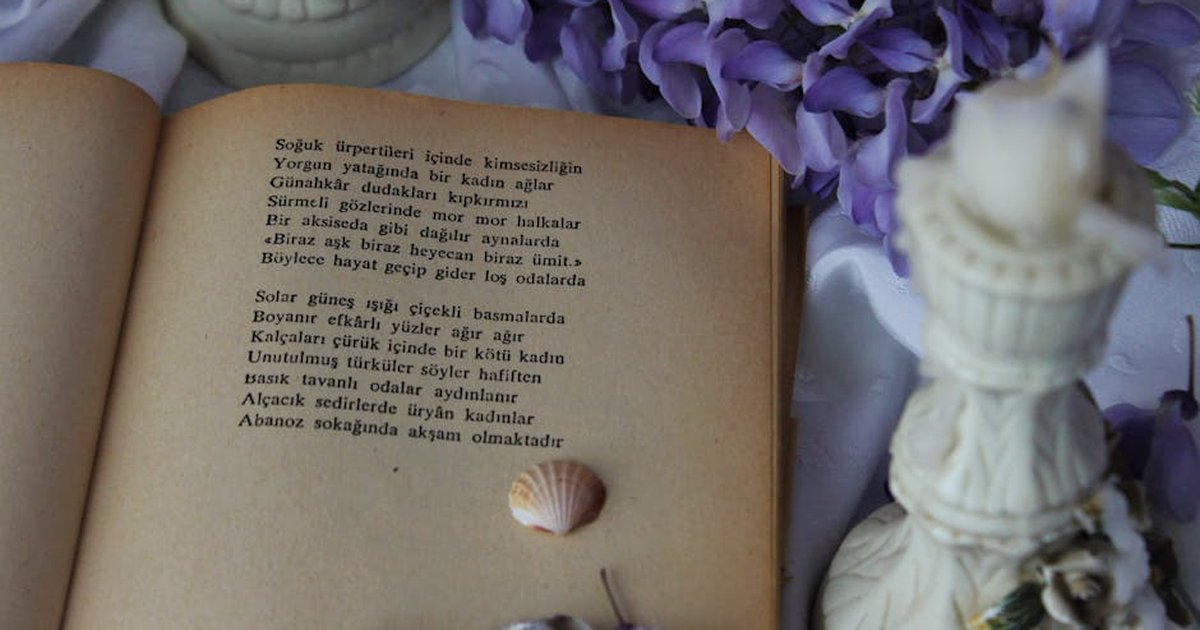 An open vintage book with poetry surrounded by purple flowers and seashells.