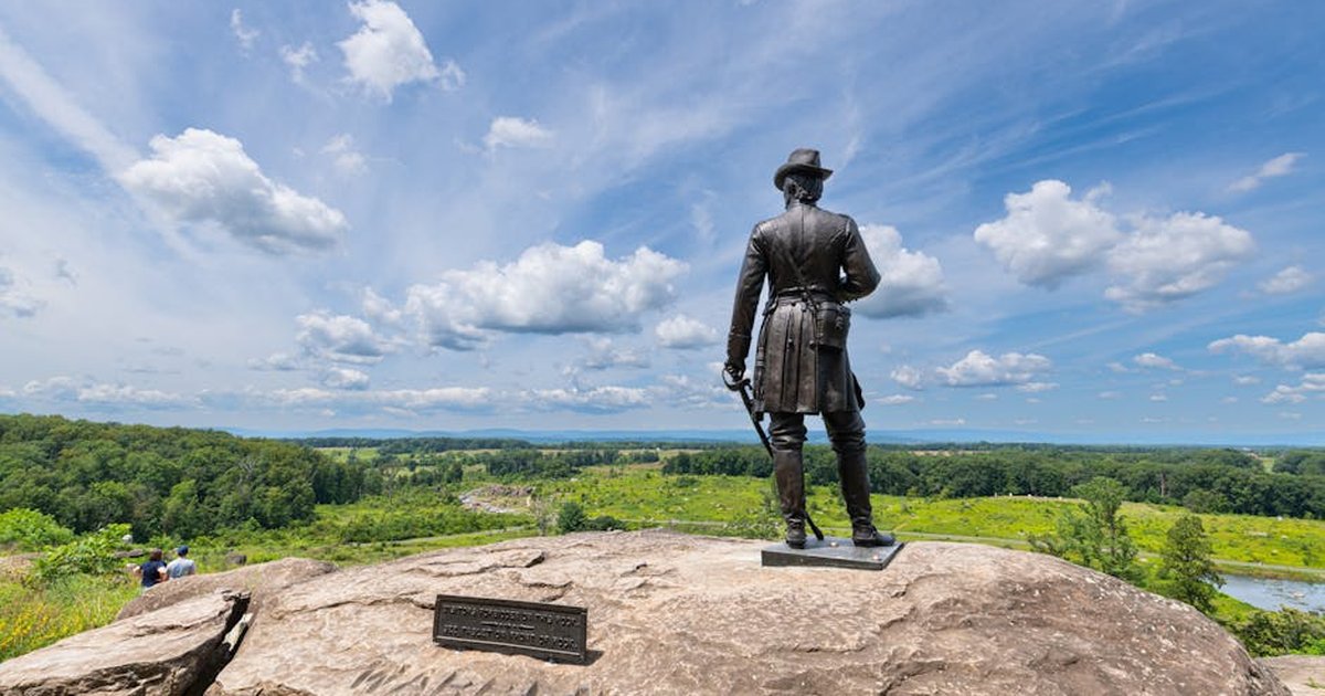 War memorial statue overlooking Gettysburg battlefield under a blue sky.