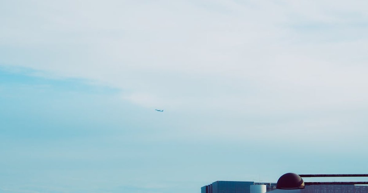 A distant airplane flies over Shinjuku City, Tokyo, with urban architecture below.