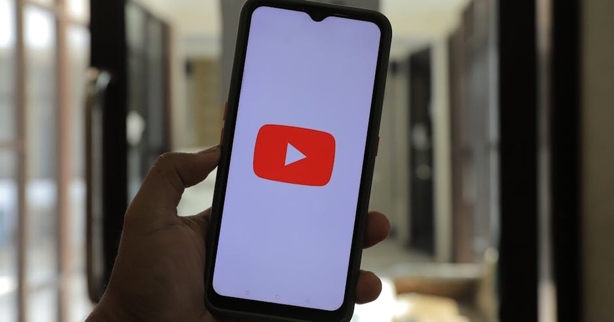 Close-up of a hand holding a smartphone displaying the YouTube logo in a well-lit room.