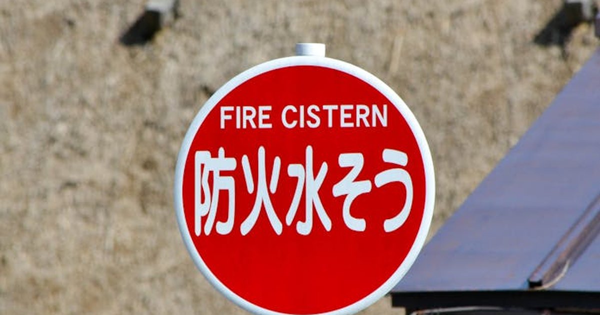 Close-up of a fire cistern sign with Japanese text against an outdoor backdrop.