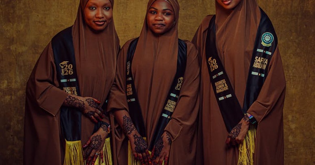 Three women in brown hijabs with henna designs wearing graduation sashes