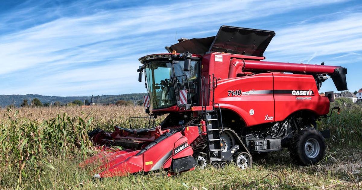 A red harvester working in a cornfield under a clear sky in rural Kassel, Germany.