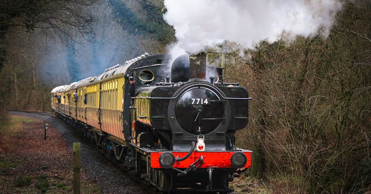 Classic steam engine 7714 travels through lush woods, showcasing railway heritage and nostalgia.