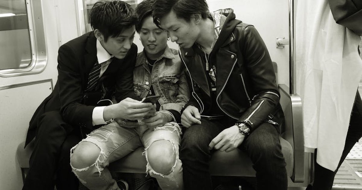 Three young men on a subway train, engaged with smartphones, sharing a moment.
