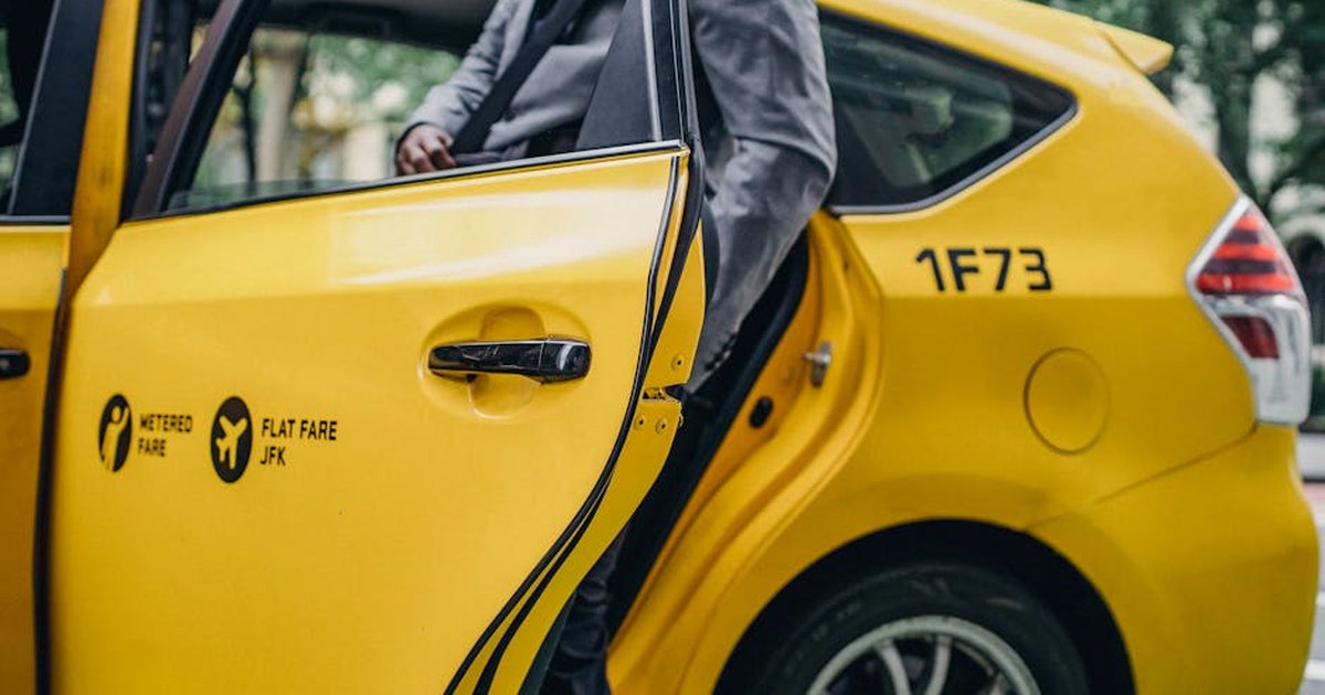 Busy crop anonymous African American male leaving modern bright yellow taxi on street of town