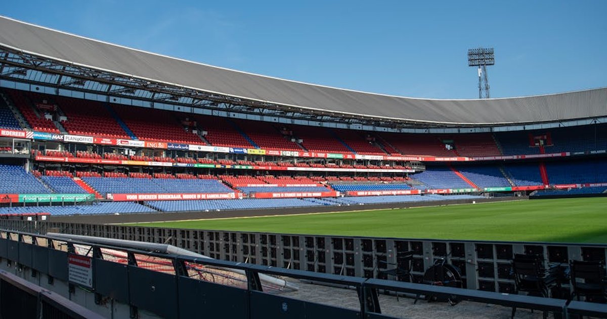Panoramic view of De Kuip stadium in Rotterdam with empty stands and a clear blue sky.