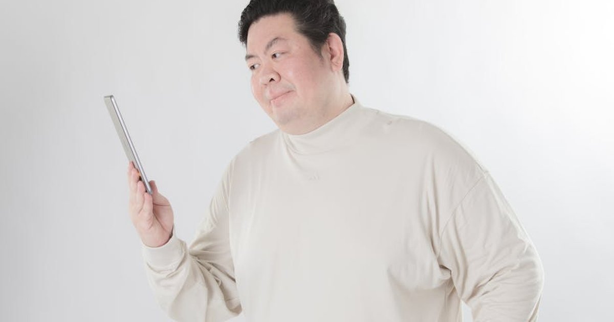 Portrait of an adult man holding a tablet device, gazing thoughtfully against a white backdrop.