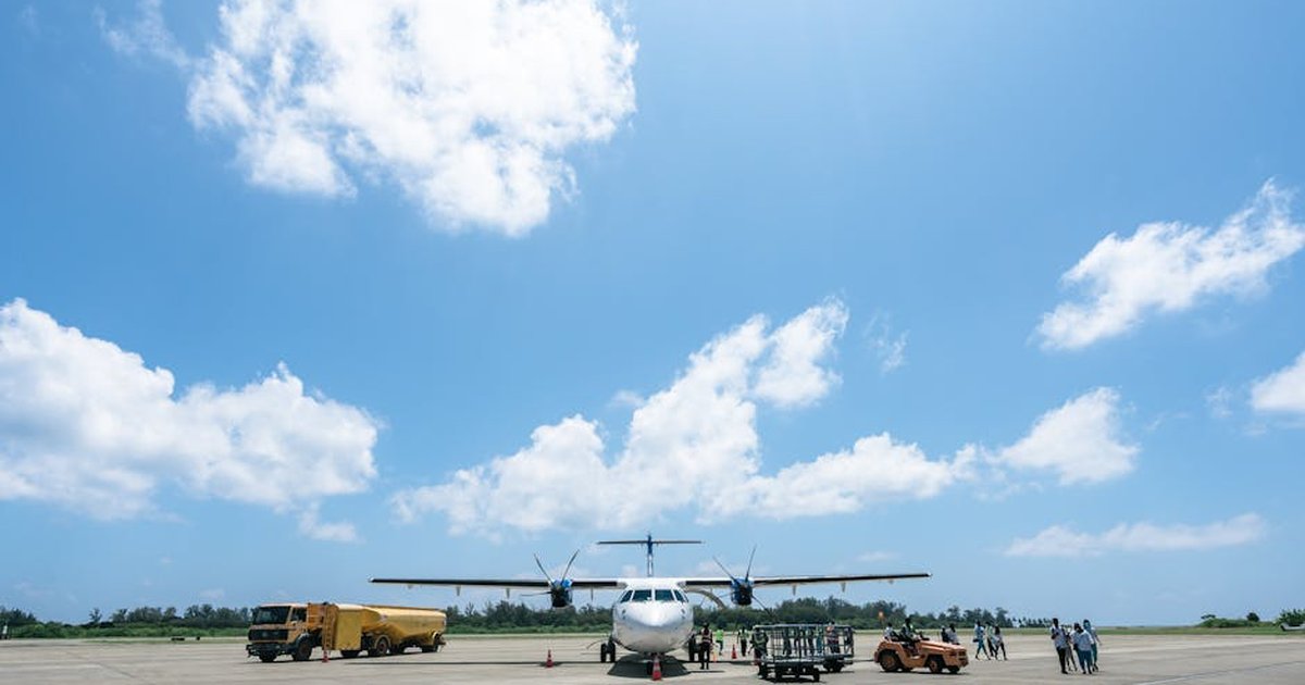 Airplane parked on airport tarmac with crew under a sunny sky.