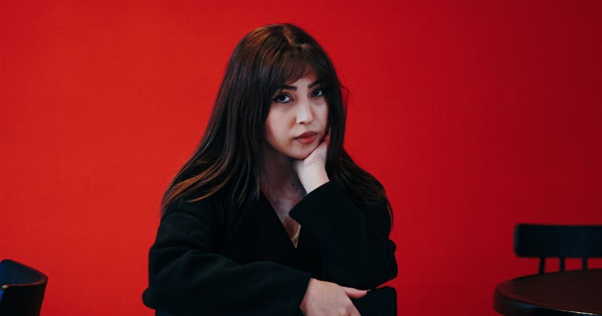 Stylish portrait of a young woman in a Tehran cafe, set against a bold red background.