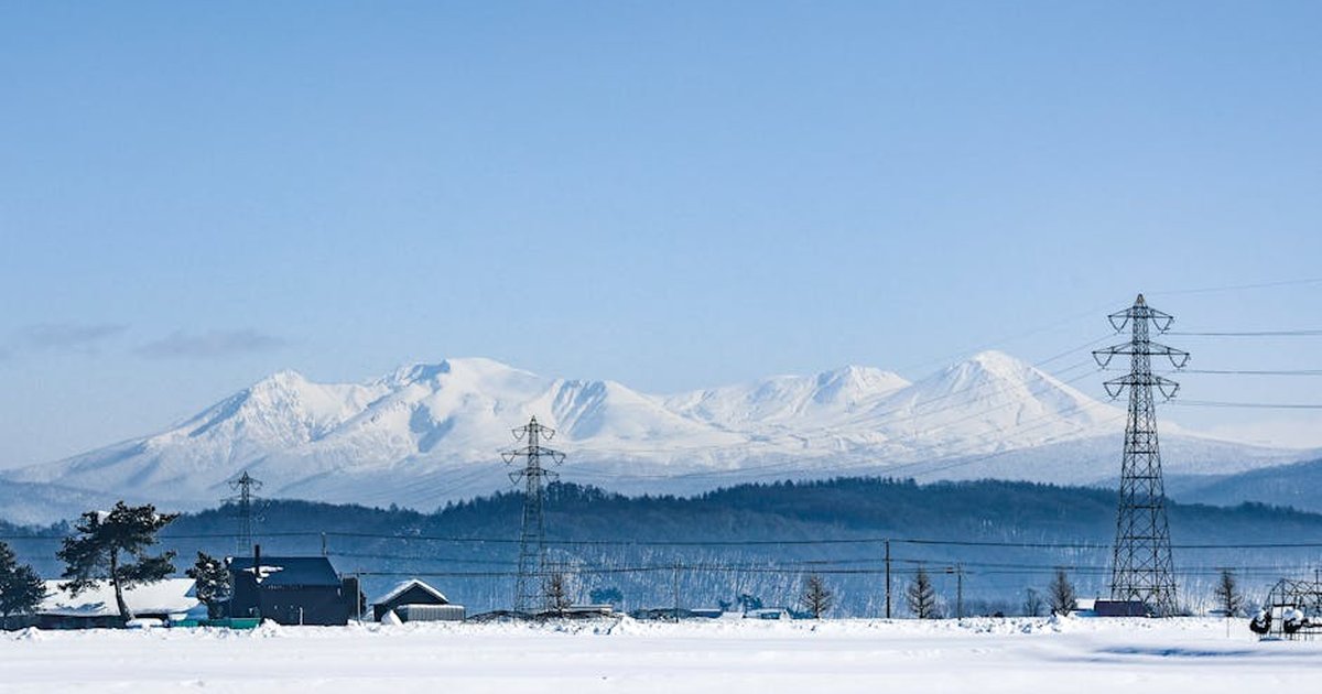 Peaceful winter scene featuring snow-capped mountains and powerlines under a clear sky.