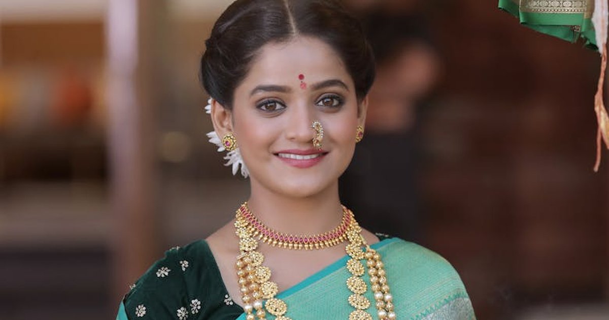 Elegant Indian woman in traditional attire with jewelry, smiling indoors.