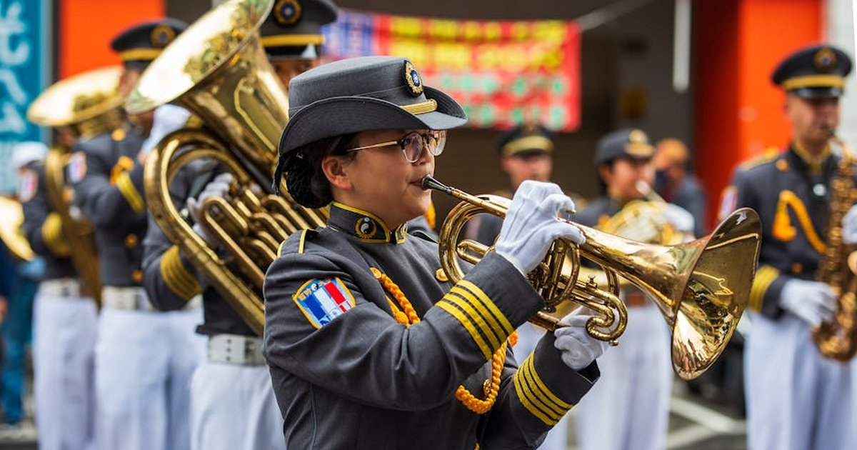 Uniformed musicians perform in a parade, featuring a trumpet player in focus.