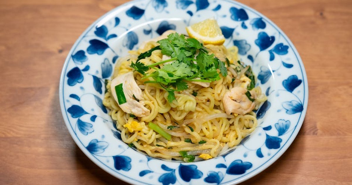 A plate of flavorful Asian stir-fry noodles garnished with herbs and lemon.